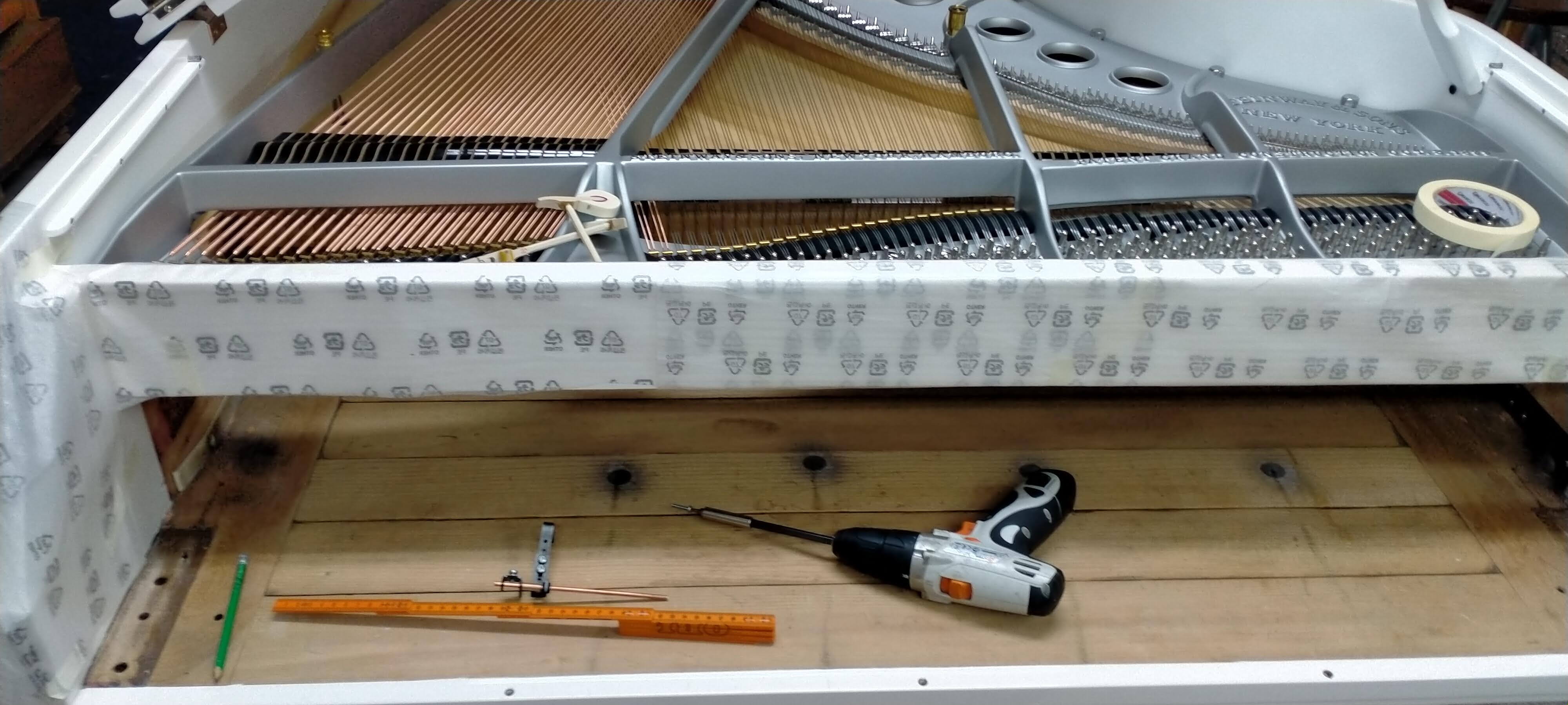 Piano de cola blanco Steinway en proceso de instalación de sistema silenciador con herramientas de trabajo